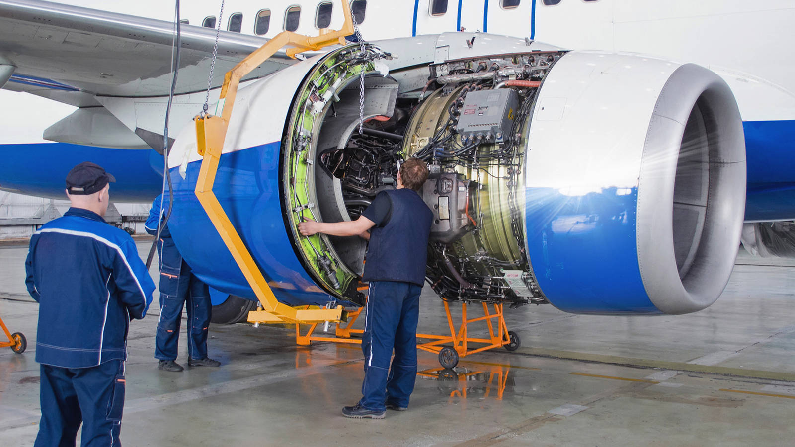 Two workers replacing an airplane engine with a device that required careful tool building measurement